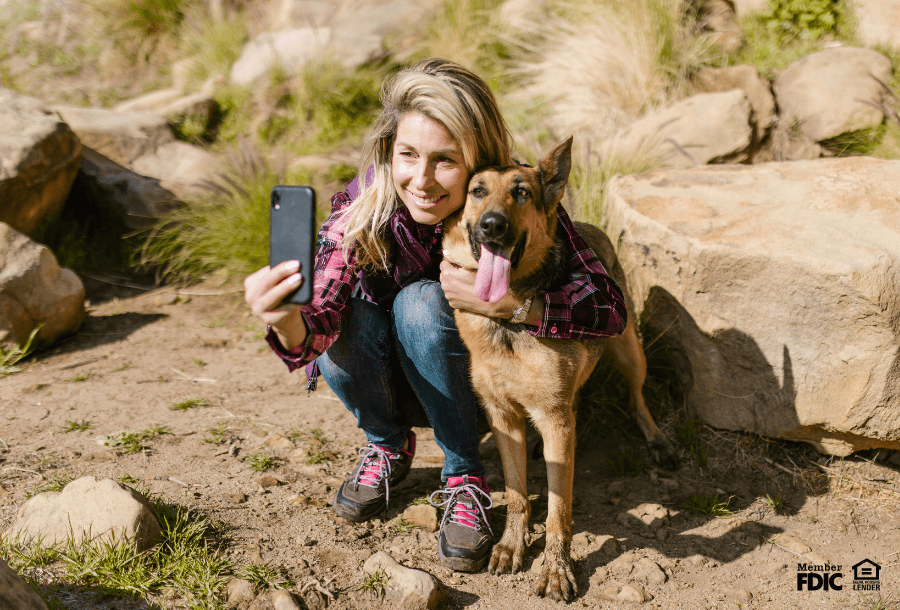 a woman poses to take a selfi with her dog while out on a hike in Denver, CO. She's saving money with a money market account.