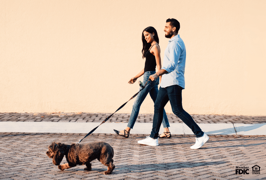 a couple walks their dog while talking about investment checking accounts.