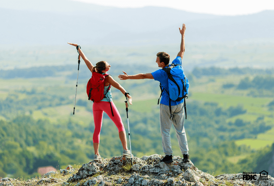 A man and woman celebrate as they summit a hill while hiking.